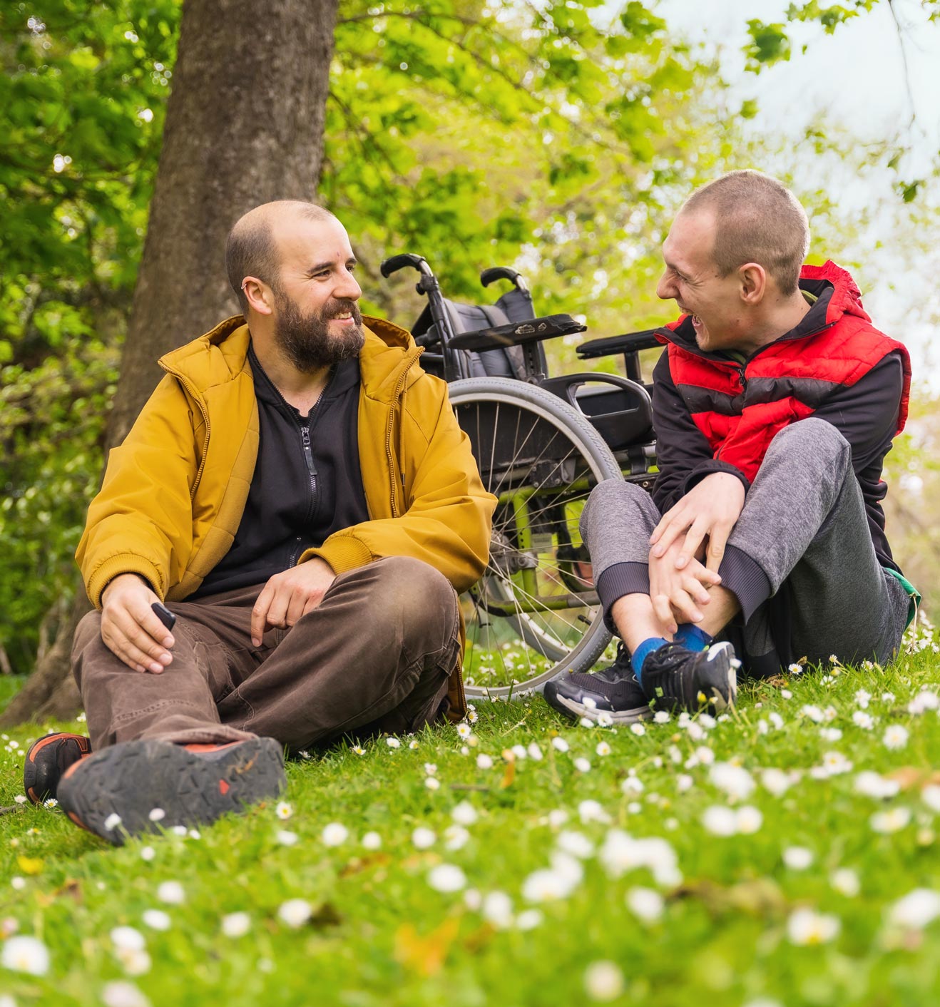 assistenz-mittelhessen Zwei Männer sitzen auf einer Wiese vor einem Rollstuhl